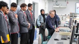 A group of five male students wearing school uniforms watch Professor Chris Stokes show them something on a computer screen.