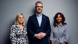 Three people stood against a grey background 
