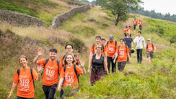 A line of people in orange t-shirts walking through greenery