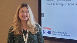 This is a picture of Jo Coster stood next to a powerpoint presentation