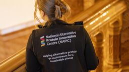 Back of woman's jacket with the text: 'National Alternative Protein Innovation Centre (NAPIC), Helping alternative proteins go mainstream for a sustainable planet'.