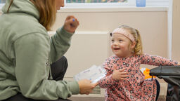 A speech and language therapist chats to a smiling young girl.
