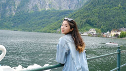 Siqing leans against a metal fence in front of a lake and looks over her shoulder at the camera