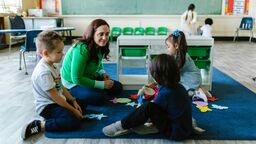 A teacher sitting on the carpet with young chilren in the classroom