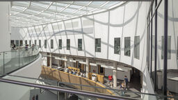 Inside a modern building - sunlight creates waves of shadow over people walking through the building