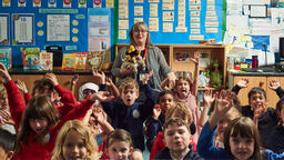 Dr Sabine Little stood with a group of children looking at the camera in a school setting at one of her previous Storytelling events.