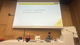Jackie Harrison, Diana Maynard and Jos Bartmann sitting behind a table under a screen displaying the title "the necessity of a safety barometer for journalists"