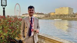 A person standing, holding a drink, with the London Eye in the background.