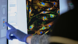 A gloved hand pointing at a screen showing research data