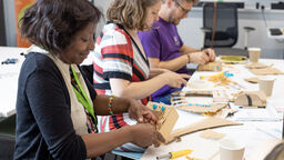 Three people sit creating musicall instruments out of cardboard and craft materials