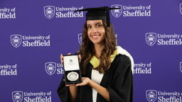 Maria Jose Gordillo Chiriboga stands in front of a purple backdrop with the University of Sheffield's logo holding the Chancellor's Medal.