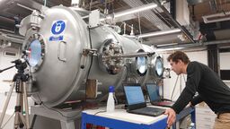 A man looks into the window of the cylindrical Large Dirty Mars Chamber, housed at the Open University.