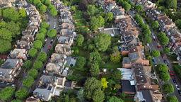 An aerial image of a UK suburban area showing curved roads, lined with houses and their tree filled gardens.