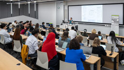 Dorothea Kleine giving a presentation at the front of a busy lecture theatre