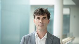 A person smiling at the camera in a grey suit.