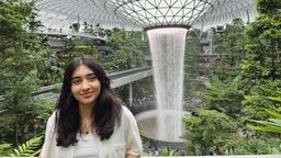 A female student stands in front of a waterfall and smiles towards the camera.