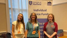 Three people smiling at the camera with a banner in the background.