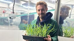 Dr Robert Caine standing holding grass