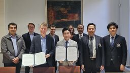 A group of nine colleagues stand in a row and smile towards the camera. Two members of staff in the centre each hold a signed document and present it towards the camera.