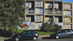 A photograph showing the exterior of a block of flats with graffiti
