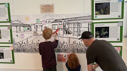 A man and two children writing on an image on a wall as part of an exhibition