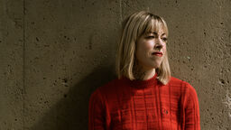 Helen Mort against a wall wearing an orange jumper 