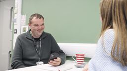 Two people sitting at a table, one smiling, holding a phone.