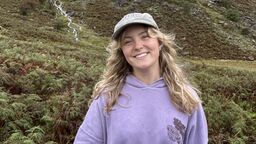 Emilia smiles at the camera she is stood in the countryside