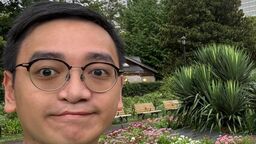 Student with short brown hair and glasses standing in park in summer