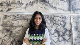 Landscape student smiling in front of charcoal drawings with arms crossed