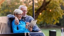 Two people sitting on a bench looking at an iPad