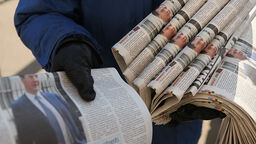 A hand holding out a newspaper from a bundle under the person's arm
