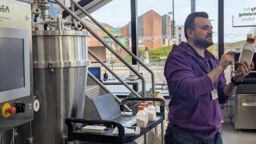A researcher wearing a purple jumper is giving a demonstration about powder processing in the pilot plant in the Diamond building