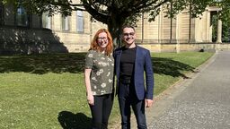 Sally and Karzan stand in Western Park in front of the museum and a tree
