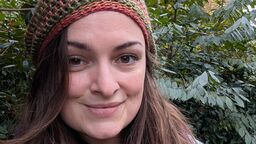 Student smiling surrounded by trees wearing hat and scarf