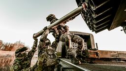 Soldiers in camouflage uniforms loading artillery equipment during a military field operation