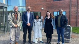 Five people stand outside a building, smiling at the camera 
