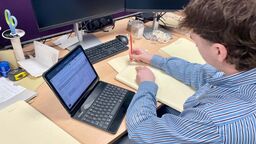 Ed sits at a laptop, making notes on a pad of paper