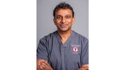 A man smiling with his arms crossed in scrubs.