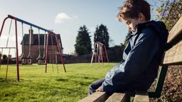 Child alone sitting on a bench with swings in the background