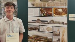 Architecture student holding certificate in front of posters of his work