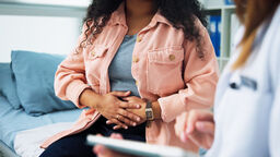 Woman holding her stomach while speaking to a doctor.