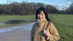 Student smiling in sunny park wearing coat and gloves 