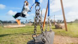 A close up on a children's swing set in a park, a young boy is using the swing but he is out of focus.